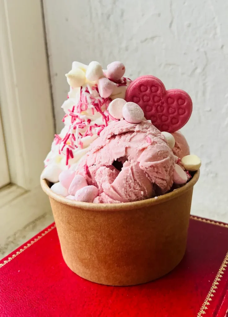 En bägare med mjukglass och rosa jordgubbsglass toppad med marshmallows, strössel och ett rosa hjärtkex på Håfveruds Glasseri.